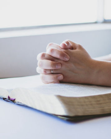 Praying hands resting on Bible